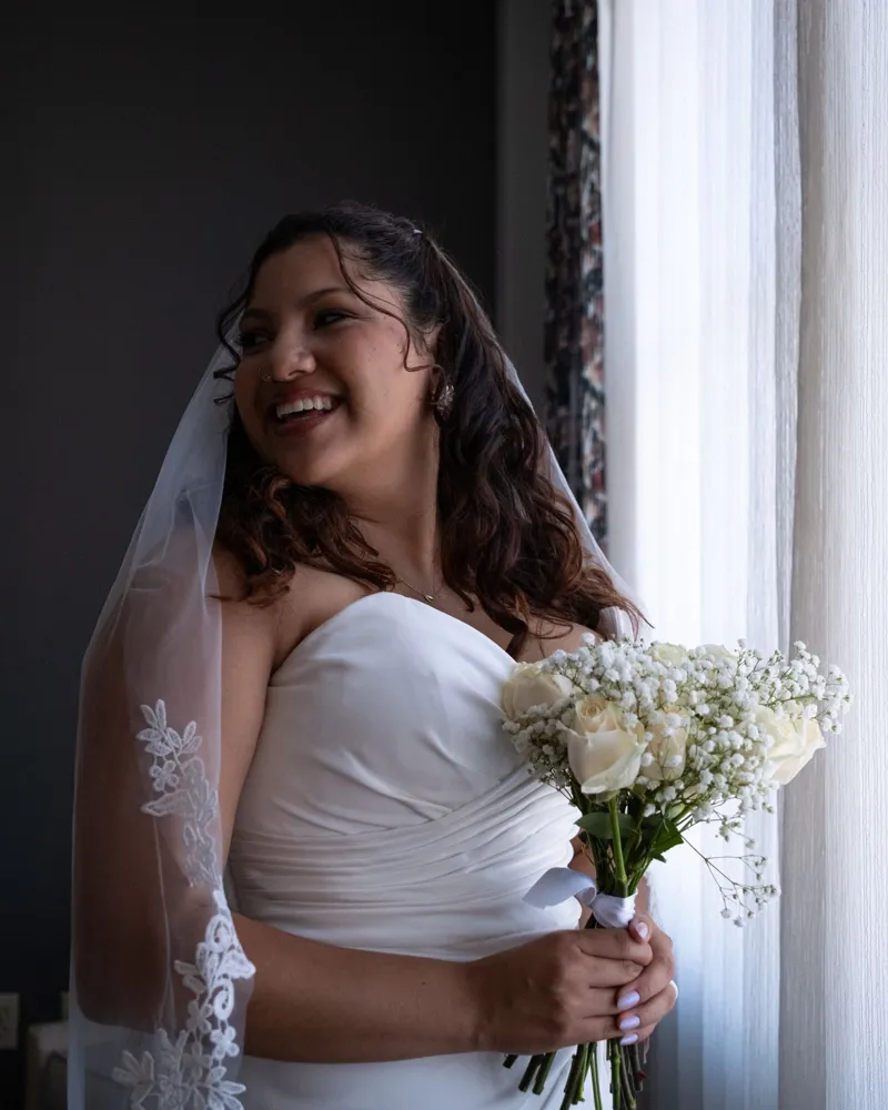 Smiling bride holding a white bouquet by the window