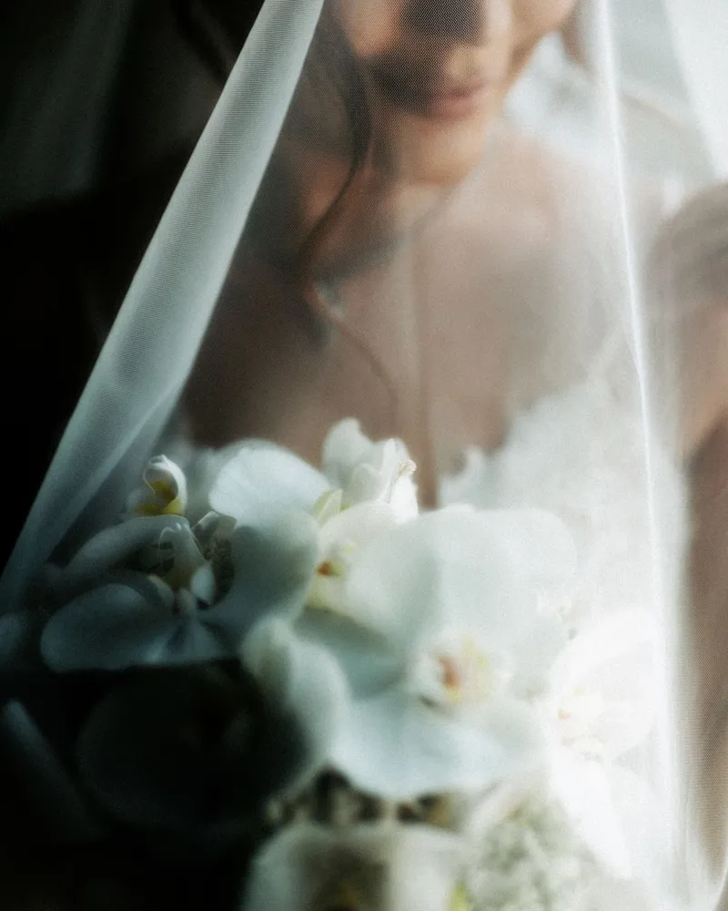 Bride under a soft veil holding white orchids