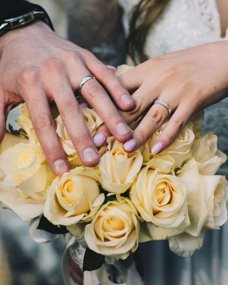 Newlyweds' hands with wedding rings over a bouquet of yellow roses